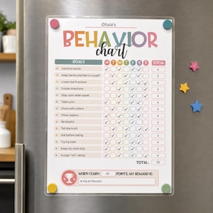 May include: A rectangular magnetic behavior chart with the title Olivia's Behavior Chart in colorful letters. It features a list of goals, a weekly tracking grid with checkmarks, and a reward section at the bottom. Four magnets hold it in place.