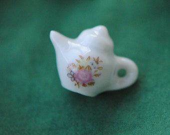 Puede incluir: Una colección de pequeñas teteras de porcelana blanca con diseños florales. Las teteras están dispuestas sobre una superficie verde.