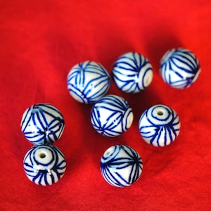 May include: Seven white ceramic beads with blue painted designs. The beads are round and have a glossy finish.