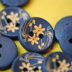 May include: A collection of blue wooden buttons with gold floral designs. Some buttons have two holes, while others have four holes.