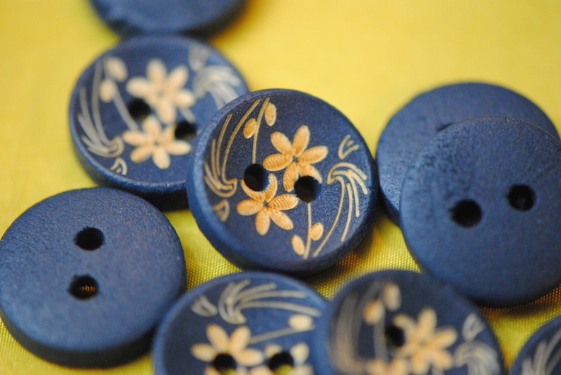 May include: A collection of blue wooden buttons with gold floral designs. Some buttons have two holes, while others have four holes.
