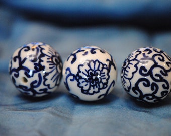Puede incluir: Tres esferas de cerámica blanca con diseños florales azules. Las esferas están dispuestas en una fila sobre un fondo de tela azul.