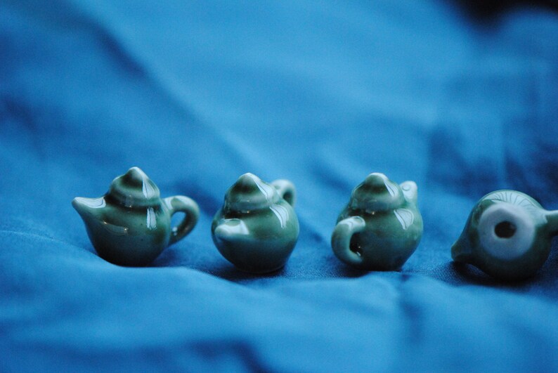 Pode incluir: Quatro pequenas chaleiras de cer&acirc;mica verde com acabamento esmaltado. As chaleiras est&atilde;o dispostas em fila sobre uma superf&iacute;cie azul.