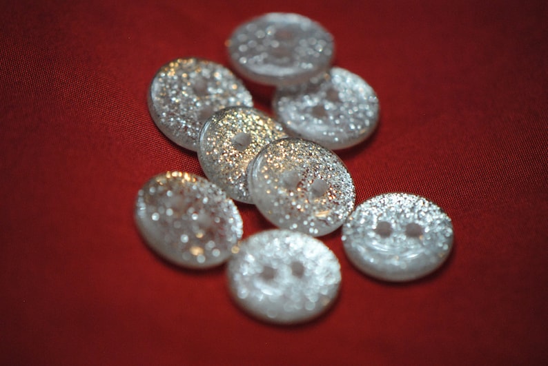 May include: A group of eight silver buttons with a textured surface. The buttons are round and have two holes each.