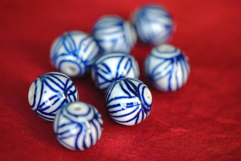 May include: A collection of blue and white ceramic beads with intricate patterns. The beads are round and have a glossy finish.