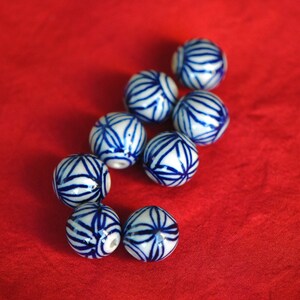 May include: A collection of eight white ceramic beads with blue floral patterns. The beads are arranged in a curved line on a red surface.