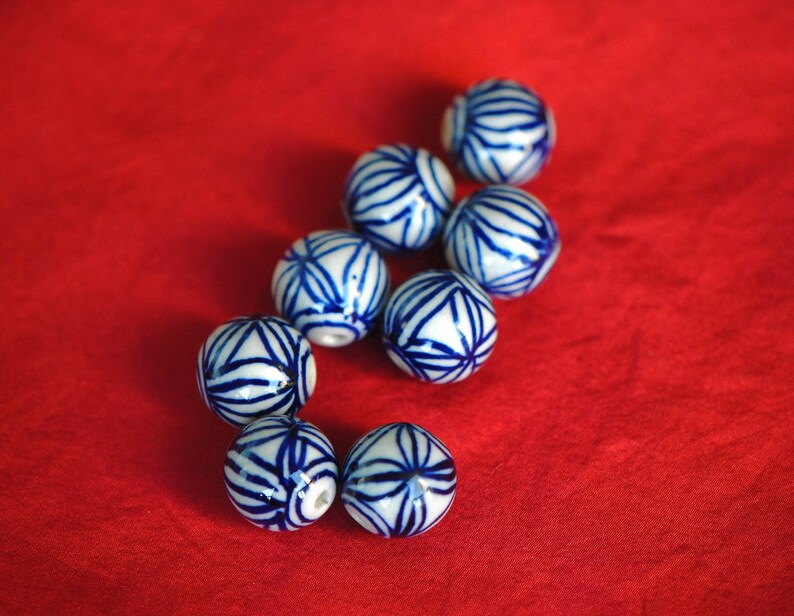 May include: A collection of eight white ceramic beads with blue floral patterns. The beads are arranged in a curved line on a red surface.