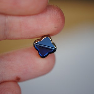 Puede incluir: Un peque&ntilde;o amuleto en forma de tr&eacute;bol de cuatro hojas con un acabado de esmalte azul oscuro y un marco de metal dorado.
