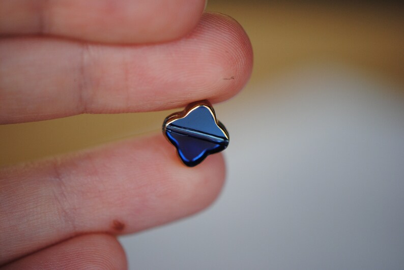 Puede incluir: Un peque&ntilde;o amuleto en forma de tr&eacute;bol de cuatro hojas con un acabado de esmalte azul oscuro y un marco de metal dorado.