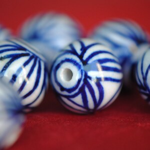 May include: A collection of white ceramic beads with blue and white patterns. The beads are round and have a glossy finish.