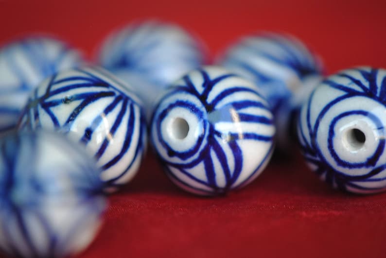 May include: A collection of white ceramic beads with blue and white patterns. The beads are round and have a glossy finish.