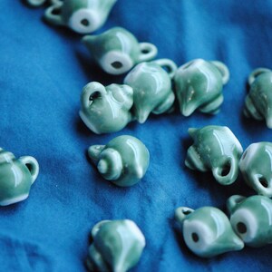 Pode incluir: Uma cole&ccedil;&atilde;o de pequenas chaleiras de cer&acirc;mica verde com detalhes brancos. As chaleiras est&atilde;o dispostas sobre uma superf&iacute;cie azul.