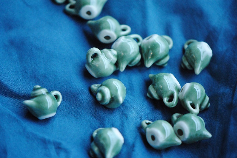 Pode incluir: Uma cole&ccedil;&atilde;o de pequenas chaleiras de cer&acirc;mica verde com detalhes brancos. As chaleiras est&atilde;o dispostas sobre uma superf&iacute;cie azul.