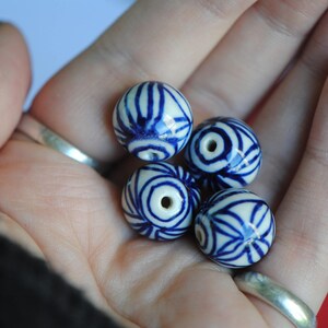 May include: Five blue and white ceramic beads with a swirling pattern. The beads are in the palm of a hand.