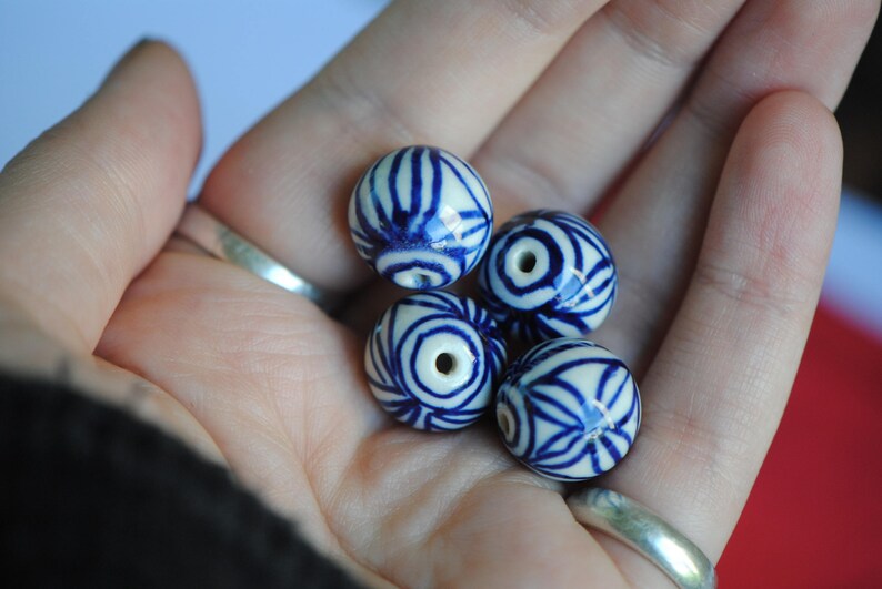 May include: Five blue and white ceramic beads with a swirling pattern. The beads are in the palm of a hand.