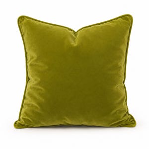 May include: A square throw cushion in a solid olive green colour. The cushion features a soft, velvet-like texture and is finished with matching green piping along all four edges, creating a defined border around the square shape of the cushion.