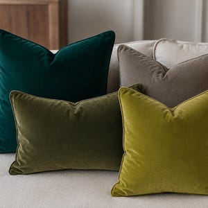 May include: A collection of four square and rectangular velvet scatter cushions in solid colours. The set includes one large dark emerald green square cushion, one medium taupe square cushion, one olive green rectangular cushion, and one lime green square cushion.
