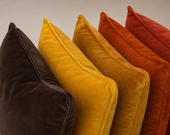 Peut inclure: Une rangée de cinq coussins carrés en velours disposés selon un dégradé de couleurs chaudes. Les teintes passent du brun foncé au jaune moutarde, jaune doré, orange brûlé et rouge profond. Chaque coussin présente des bords passepoilés.