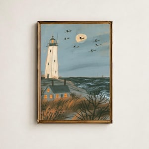 Op de afbeelding: Een ingelijst schilderij met een witte vuurtoren en een klein huis met gloeiende oranje ramen op een rotsachtige kust. De scène toont een blauwe lucht met een bleke maan en verschillende donkere silhouetten van figuren op bezemstelen.