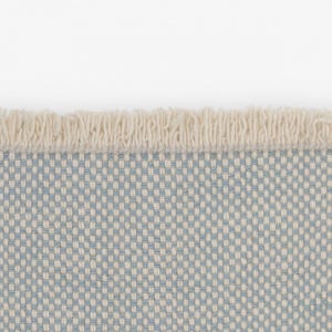 Pode incluir: Um tecido com um padr&atilde;o de grelha repetitivo de fios azul-claros e branco-sujo. A extremidade do tecido &eacute; rematada com uma fila de franjas curtas e densas de cor branco-sujo que se estendem horizontalmente pelo topo do material.