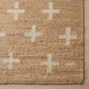 Puede incluir: Una alfombra tejida de fibras naturales de color tostado con un patrón repetitivo de signos más blancos. La alfombra tiene una superficie gruesa y texturizada con un tejido trenzado visible y un borde de acabado a lo largo del lado de la alfombra.