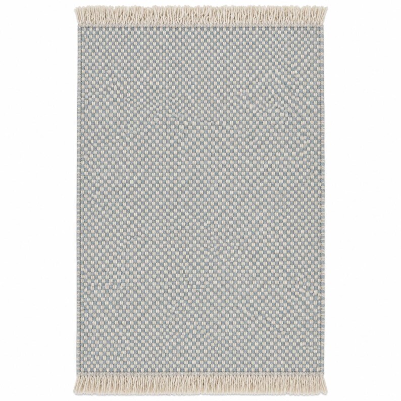 Pode incluir: Um tapete retangular com um padr&atilde;o geom&eacute;trico repetitivo de pequena escala em azul claro e branco sujo. O tapete tem uma superf&iacute;cie tecida texturizada e &eacute; rematado com franjas curtas de cor creme nas extremidades superior e inferior.