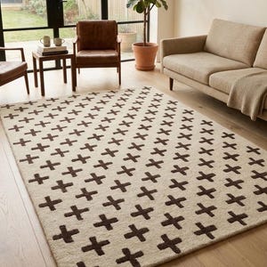 Puede incluir: Una alfombra rectangular que presenta una base de color crema con un patrón repetitivo de símbolos en forma de cruz de color marrón oscuro dispuestos en líneas diagonales por toda la superficie del revestimiento.
