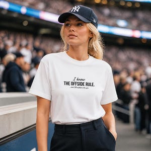 Puede incluir: Una camiseta blanca con el texto "I know THE OFFSIDE RULE...and I'll explain it to you." se usa con una gorra de béisbol azul marino con un logotipo blanco. La persona lleva pantalones negros.
