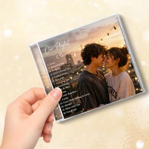 Puede incluir: Una caja de CD de plástico transparente con una portada personalizada que muestra una fotografía de una pareja al atardecer. El texto Our Playlist está impreso en la parte superior, seguido de una lista numerada de dieciséis canciones.