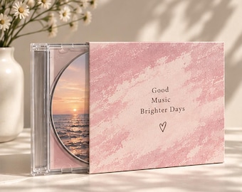 Op de afbeelding: Een doorzichtig plastic cd-doosje met een roze, gestructureerde hoes met de tekst Good Music Brighter Days en een klein hartje. De zichtbare cd-inlay toont een zonsondergang boven de oceaan met een kalme zee en een heldere horizon.