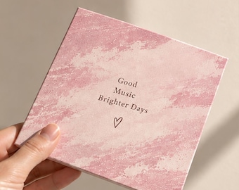 Op de afbeelding: Een vierkante, platte kaart in roze tinten met een gestructureerd penseelstreekpatroon. In het midden staat de donkerbruine tekst "Good Music Brighter Days" gevolgd door een klein, handgetekend hartsymbool. De kaart heeft een matte afwerking.