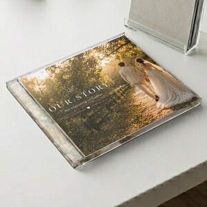 May include: A clear acrylic photo album with the words "OUR STORY the beginning of forever" printed on the cover. The album features a photograph of a couple walking down a path. The album is on a white surface.