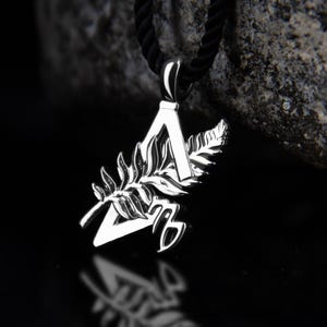 May include: A silver-toned metal pendant featuring a triangular frame, a detailed fern leaf overlay, and a Virgo zodiac symbol at the base. The pendant is suspended from a thick black cord, showcasing a polished finish with sharp, reflective edges.