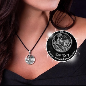 May include: A silver pendant necklace with a detailed circular charm. The charm features a woman with a wreath, surrounded by harvest imagery. The pendant hangs from a black cord. The text "Energy of Fruitfulness, Creation" is visible.