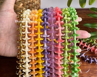 May include: A collection of multi-colored beaded strands featuring small, flower-shaped components in gold, cream, orange, yellow, purple, pink, and green. The strands are arranged vertically, displaying a repeating floral pattern throughout.