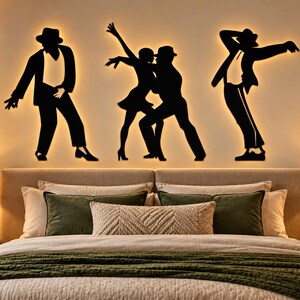 Peut inclure: Un ensemble de trois silhouettes murales noires représentant des personnages dans des poses de danse, incluant un danseur seul à gauche, un couple au centre et un danseur seul à droite, le tout éclairé par un rétroéclairage chaud au mur.