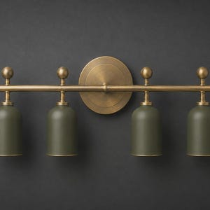 以下が含まれることがあります： 中央に円形のバックプレートを備えた水平な真鍮製のバーが特徴の壁掛け照明器具。マットなオリーブグリーンのベル型シェードが4つバーから吊り下げられており、それぞれ小さな真鍮製の球体フィニアルと真鍮の金具で装飾されています。