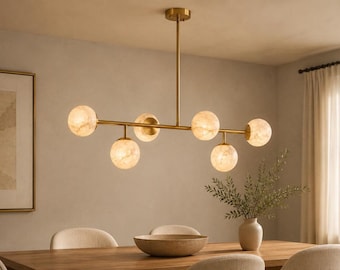 May include: A linear chandelier featuring a horizontal brass-toned metal rod suspended from the ceiling, holding six spherical light globes with a marbled, off-white texture that emit a soft, warm glow throughout the interior space.