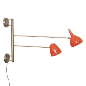 Peut inclure: Une applique murale moderne du milieu du siècle avec deux abat-jours coniques orange réglables. La lampe a une finition en laiton et un cordon électrique noir. Les abat-jours ont de petites perforations.