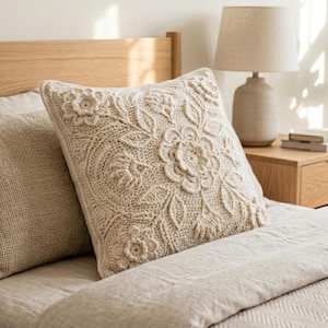 May include: A bed with a light-coloured wooden headboard and bedding. Two pillows are visible, one with a textured, floral design and the other with a plain weave. A lamp and a small bedside table are also in the image.