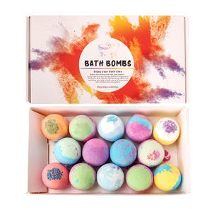 Puede incluir: Un juego de cajas de bombas de baño coloridas. La tapa de la caja presenta las palabras "BATH BOMBS" en un círculo con una ilustración de bañera y un diseño de salpicaduras coloridas. La caja contiene 14 bombas de baño esféricas de varios colores.