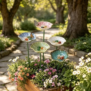 Peut inclure: Cinq tuteurs de jardin en céramique en forme de fleur, de couleurs rose, bleu, vert clair, blanc et sarcelle, montés sur de fines tiges métalliques vertes. Le cœur des fleurs contient des galets en verre colorés et deux papillons sont posés.