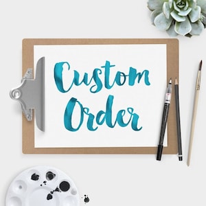 May include: A white clipboard with a brown frame holds a white sheet of paper with the words "Custom Order" written in blue watercolor.