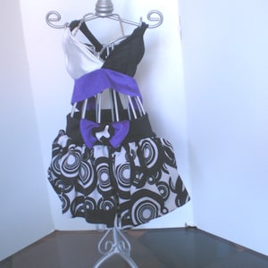 May include: A black and white patterned skirt with a purple and white top on a silver mannequin stand.