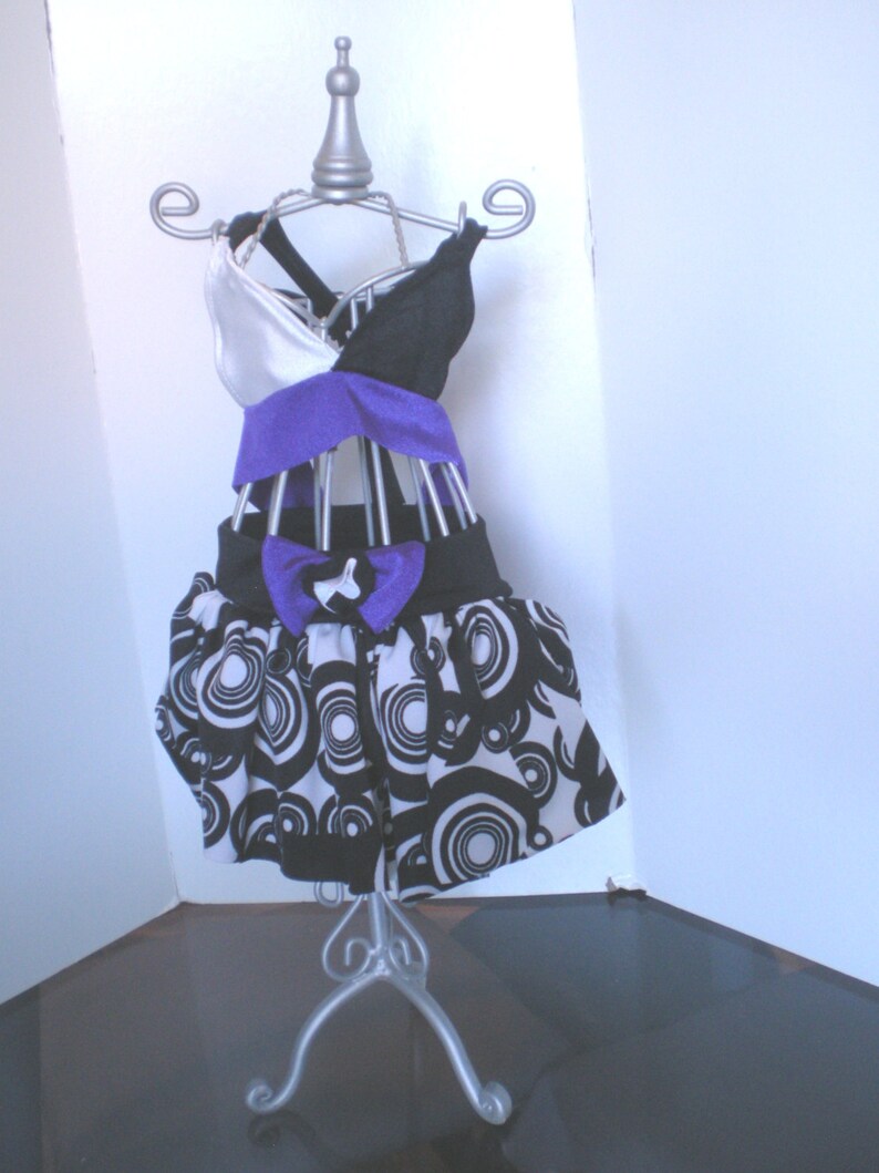 May include: A black and white patterned skirt with a purple and white top on a silver mannequin stand.