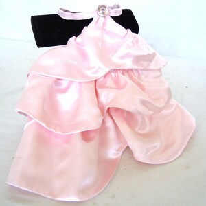 May include: A pink satin ruffle collar with a rhinestone embellishment. The collar is displayed on a black velvet stand.