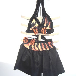 May include: A black and orange tiger print dance costume with a halter top and a black skirt. The top has a black bow in the center and the skirt has a black and orange tiger print band at the top.