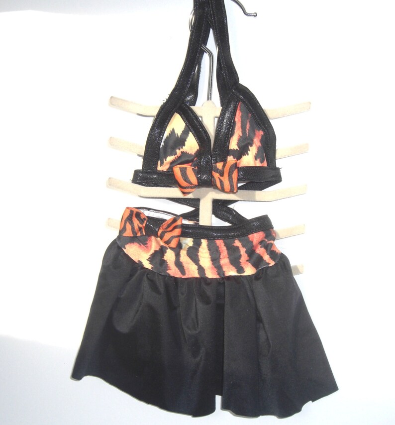 May include: A black and orange tiger print dance costume with a halter top and a black skirt. The top has a black bow in the center and the skirt has a black and orange tiger print band at the top.