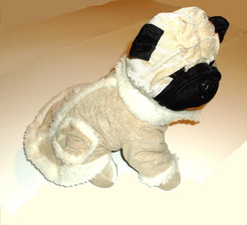 Puede incluir: Un juguete de peluche de un carlino que lleva un abrigo de piel marr&oacute;n y blanco con capucha. El juguete tiene ojos negros y una nariz negra.