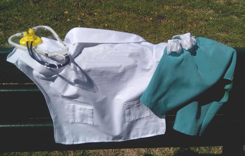 May include: A white medical lab coat with two pockets and a teal scrub set. A stethoscope with a yellow and clear plastic head is draped over the coat. The items are arranged on a dark green bench.